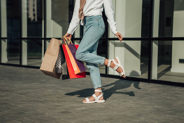 Retrato de la señora europea de la mano bolsas coloridas mujer después de comprar en camisa blanca jeans tienda al por menor cerca del centro comercial en las ventas callejeras negro viernes temporada bokeh fondo - Foto, Imagen