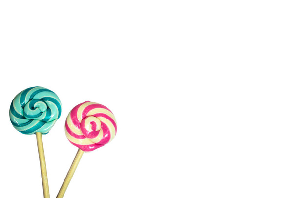 Dos piruletas dulces con rayas de color rojo, azul, turquesa y blanco en espiral sobre un palo de madera aislado sobre un fondo blanco. Tarjeta de vacaciones. Concepto de cumpleaños, lugar para el texto. - Foto, imagen
