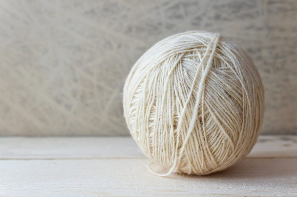 White ball of yarn on a wooden table over vintage wallpaper - Zdjęcie, obraz