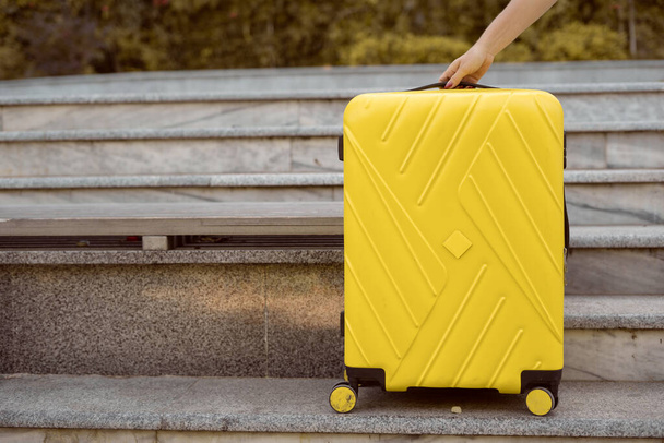 Μια κίτρινη βαλίτσα με ρόδες στέκεται στις σκάλες. Αποσκευές και χειραποσκευές όταν ταξιδεύετε. - Φωτογραφία, εικόνα