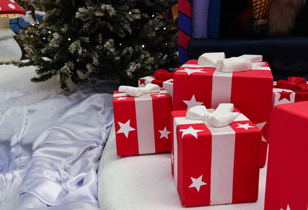 Er liggen veel rood-witte geschenkdozen onder de kerstboom. Cadeaus liggen onder de boom. Ongebruikelijke geschenken voor de vakantie. - Foto, afbeelding