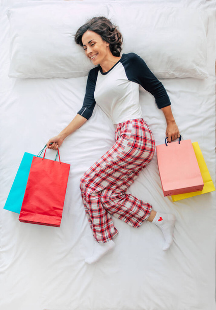 Top view full-length photo of a beautiful young curly brunette woman in casual clothes with shopping bags and credit card in hands. Dreaming about shopping in a mall. Black Friday - Fotografie, Obrázek