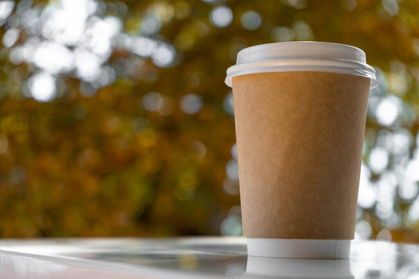 Papír eldobható kávéscsésze egy fehér asztalon őszi bokeh. - Fotó, kép