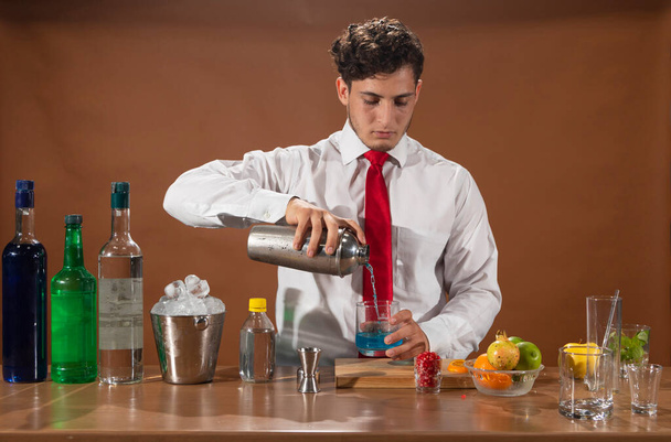 Barman preparing alcoholic drink with a cocktail shaker at the bar with some glasses of liqueur.  - Foto, Imagem