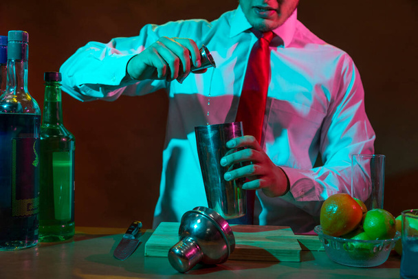 Barman preparing alcoholic drink with a cocktail shaker at the bar with some glasses of liqueur.  - Foto, imagen