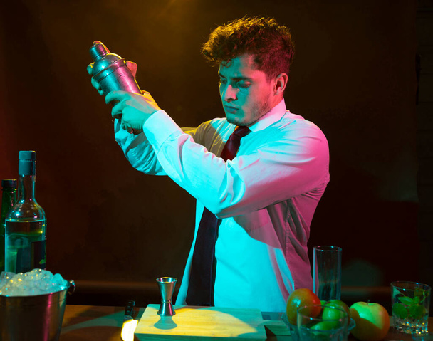 Barman preparing alcoholic drink with a cocktail shaker at the bar with some glasses of liqueur.  - Fotó, kép