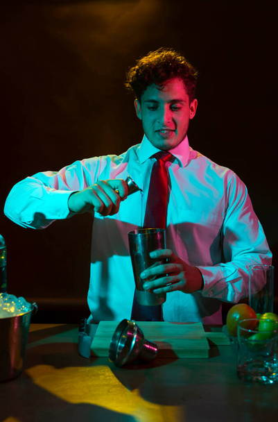 Barman preparing alcoholic drink with a cocktail shaker at the bar with some glasses of liqueur.  - Photo, Image