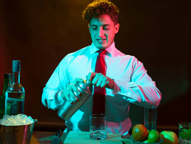 Barman preparing alcoholic drink with a cocktail shaker at the bar with some glasses of liqueur.  - Fotó, kép