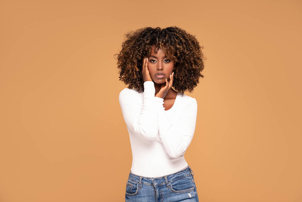 Young beautiful and fashionable african woman with afro hair, wearing casual clothes, posing over beige studio background. - Fotografie, Obrázek