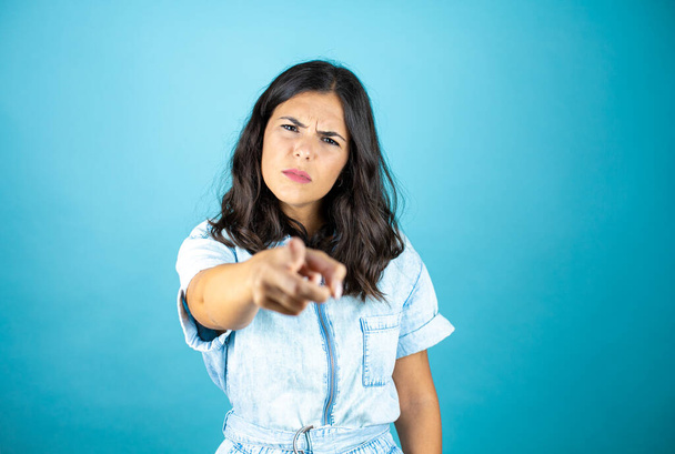 Young beautiful woman wearing a denim jumpsuit over isolated blue background pointing to the front with finger. - Photo, Image