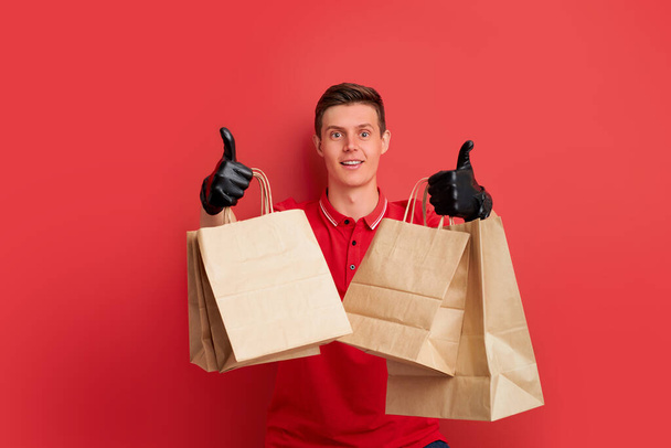 caucasian delivery man employee in red t-shirt uniform hold craft paper packet with food isolated - Foto, immagini