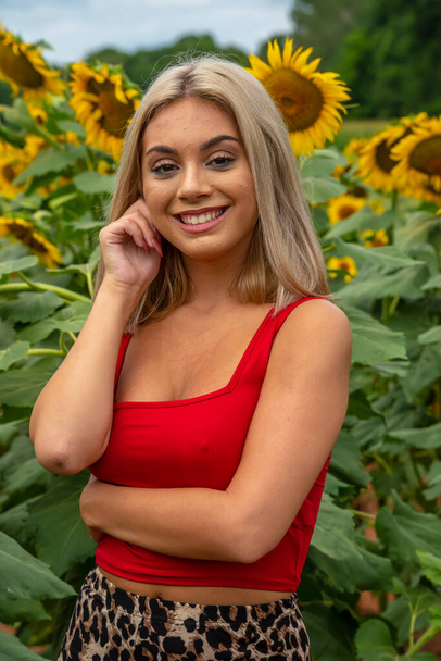 Une magnifique jeune mannequin blonde pose à l'extérieur dans un champ de tournesols tout en profitant d'une journée estivale - Photo, image