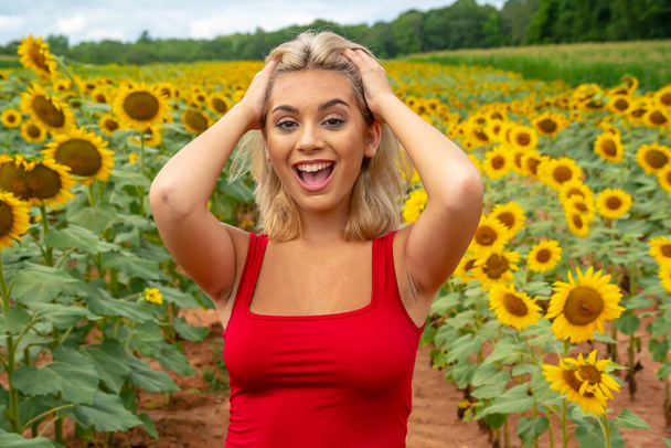 Een prachtig jong blond model poseert buiten in een veld van zonnebloemen terwijl u geniet van een zomerse dag - Foto, afbeelding