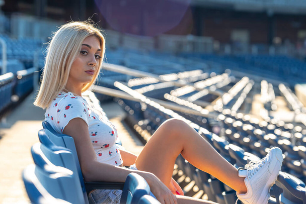 Wspaniała młoda blondynka modelka pozuje na zewnątrz, ciesząc się letnim dniem na stadionie przed meczem - Zdjęcie, obraz