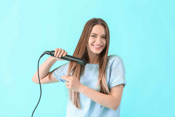 Young woman with straightening iron on color background - Foto, imagen