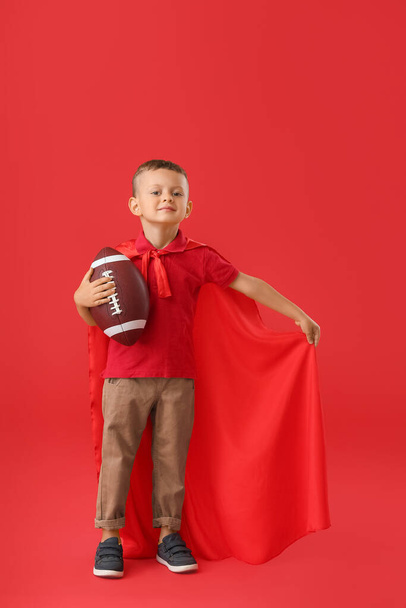 Kleine jongen met rugby bal en mantel op kleur achtergrond - Foto, afbeelding