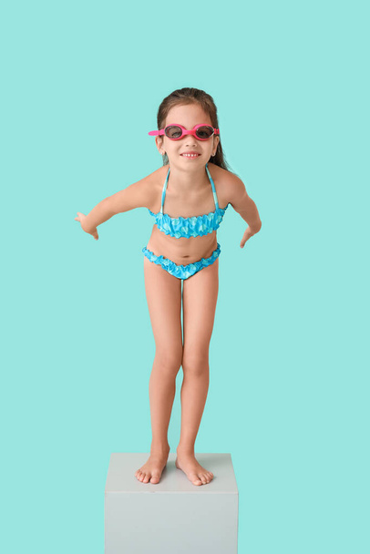 Little girl in start position on swimming block against color background - Φωτογραφία, εικόνα
