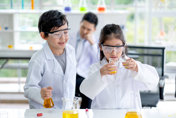 Malý chlapec se dívá na holčičku nalít nějaké barevné chemikálie do baňky v laboratoři třídy místnosti. Koncepce správné praxe a vzdělávání vědy pro děti podporují jejich učení. - Fotografie, Obrázek