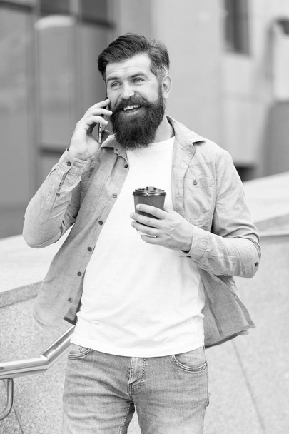 Kahvia ja puhetta. Onnellinen hipsteri puhuu puhelimessa kahvin äärellä. Takeaway-kahvia. Kahvitauko. Modernia elämää. Modernia teknologiaa. Nykyaikainen kommunikaatio. Nykyajan tasalla pysyminen - Valokuva, kuva