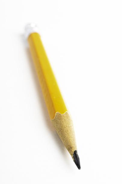 Κοντινό πλάνο ή μακρό πλάνο με επιλεκτική εστίαση ενός οξυνισμένου κλασικού κίτρινου-πορτοκαλί εξαγωνικού μολυβιού stub σε απλό λευκό χαρτί. - Φωτογραφία, εικόνα