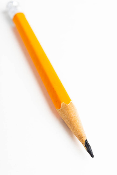 Közelkép vagy makró felvétel egy élezett, klasszikus sárga-narancssárga hatszögletű ceruzadarab szelektív fókusszal, sima fehér papírra rögzítve. - Fotó, kép