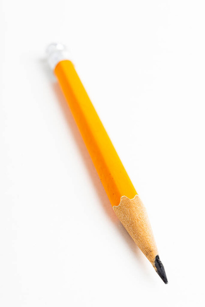 Közelkép vagy makró felvétel egy élezett, klasszikus sárga-narancssárga hatszögletű ceruzadarab szelektív fókusszal, sima fehér papírra rögzítve. - Fotó, kép