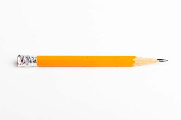 A close-up or macro shot with selective focus of a sharpened classic yellow-orange hexagonal pencil stub set on plain white paper. - Photo, Image