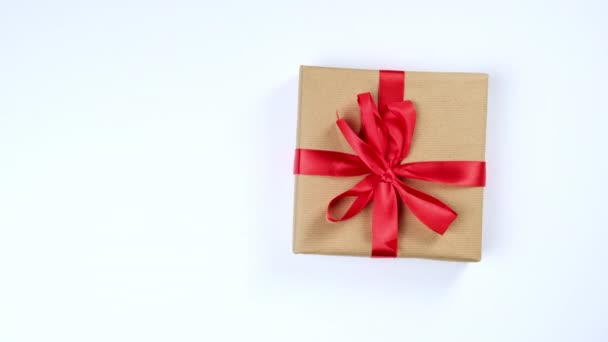 női kéz tesz ajándékokat csomagolt barna kraft papír egy fehér asztal, felső nézet - Felvétel, videó