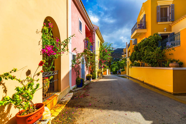 Traditional street with greek houses with flowers in Assos, Kefalonia island. Traditional colorful greek houses in Assos village. Blooming fuchsia plant flowers. Kefalonia island, Greece - Photo, Image