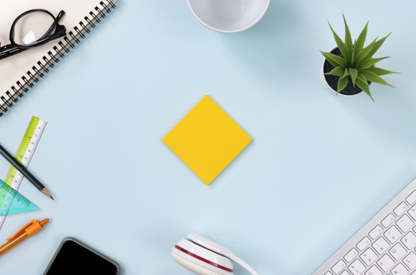 Yellow Sticky Note or Note Pad and Office Supplies as Keyboard, Pen, Pencil, Office Plants, Notebook, Glasses, Smartphone, Headphone, Coffee Cup on Modern Clean Creative Office Desk or Table on Top View - Foto, imagen