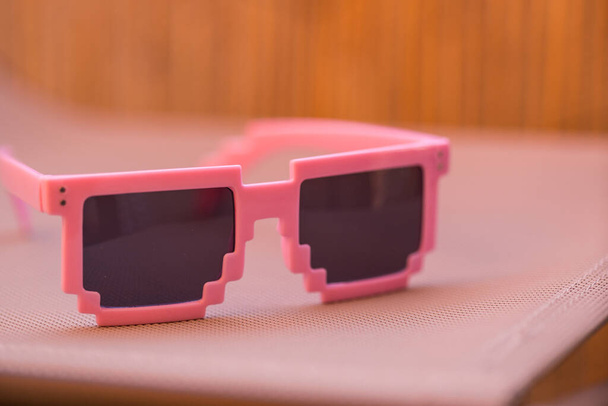 Рожеві піксельні сонцезахисні окуляри модель з чорними лінзами крупним планом в літній день. Вибірковий фокус
 - Фото, зображення