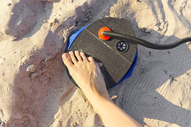 Жінка з повітряною ногою накачує надувний матрац або повітряне ліжко на піщаному пляжі. Фут надуває повітряний матрац ножний насос на пісок
. - Фото, зображення