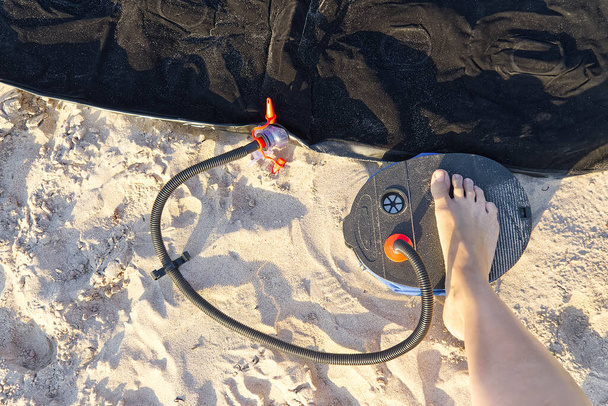 空気足ポンプを備えた女性は、砂のビーチで膨脹可能なマットレスまたはエアベッドをポンプします。足は砂の上に足ポンプで空気マットレスを膨らませます. - 写真・画像