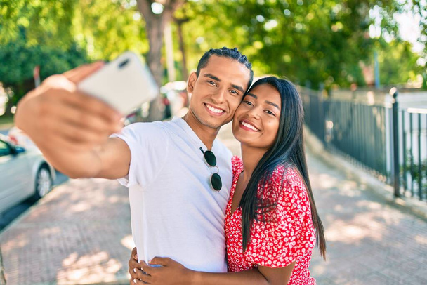 Молодая латинская пара улыбается счастливая делая селфи на смартфоне на улице города. - Фото, изображение
