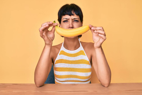 Brunetka nastolatka trzyma banana jak zabawny uśmiech napuchnięte policzki z zabawną twarzą. usta napompowane powietrzem, łapie powietrze.  - Zdjęcie, obraz