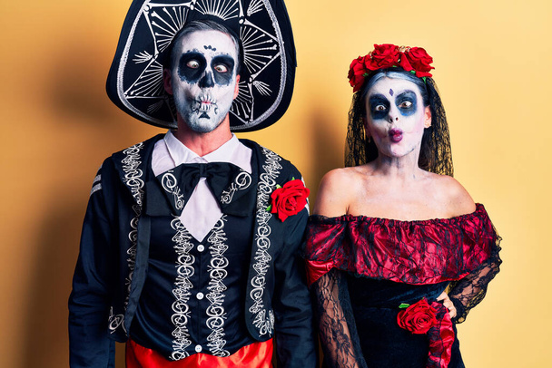 Jeune couple portant le jour mexicain du costume mort sur jaune faisant visage de poisson avec des lèvres, geste fou et comique. expression drôle.  - Photo, image