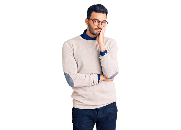 Νεαρός όμορφος Ισπανός άνδρας φορώντας κομψά ρούχα και γυαλιά σκεπτόμενος κουρασμένος και βαριεστημένος με προβλήματα κατάθλιψης με σταυρωμένα χέρια.  - Φωτογραφία, εικόνα