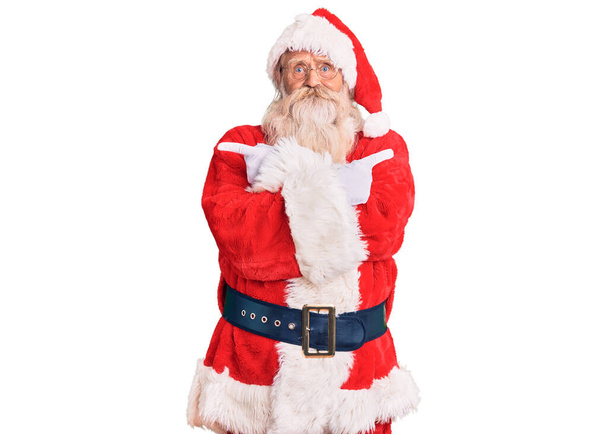 Alter älterer Mann mit grauen Haaren und langem Bart in traditioneller Weihnachtsmanntracht, der mit den Fingern nach beiden Seiten zeigt, verschiedene Richtungen widersprechen  - Foto, Bild