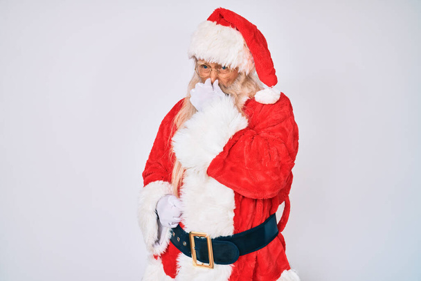 Staruszek z siwymi włosami i długą brodą w kostiumie Świętego Mikołaja z szelkami wąchający coś śmierdzącego i obrzydliwego, nieznośnego, wstrzymujący oddech palcami na nosie. nieprzyjemny zapach  - Zdjęcie, obraz