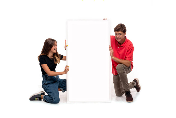 Studio laukaus hymyilevä nuori poika ja tyttö tilalla valkoinen mainostaulu kopioi tilaa valkoista taustaa vasten - Valokuva, kuva