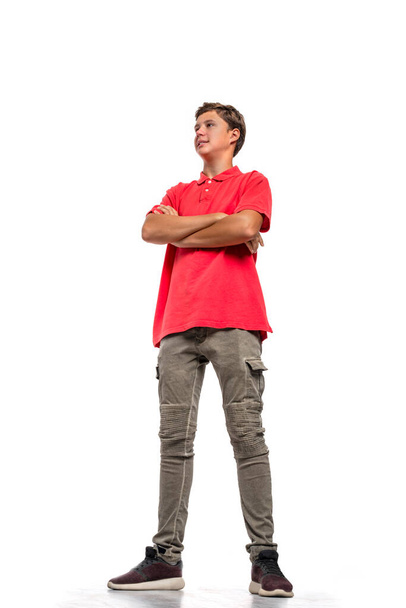 Pełna długość portret młodego chłopca nastolatka z ramionami przez noszenie czerwonej koszuli na białym tle w studio.  - Zdjęcie, obraz