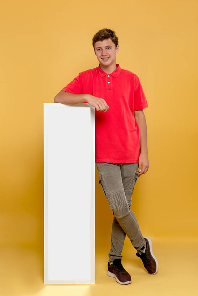 Stúdió lövés mosolygós fiatal fiú kezében fehér óriásplakát fénymásoló hely sárga háttér - Fotó, kép