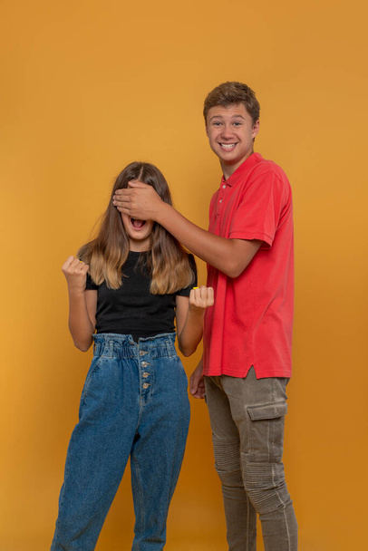 Tourné d'adolescents drôles, garçon et fille, triant les choses d'une manière plaisante sur fond jaune en studio - Photo, image