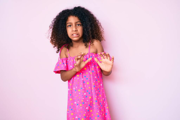 Afroamerikanisches Kind mit lockigem Haar trägt legeres Kleid angeekelten Ausdruck, unzufrieden und ängstlich dabei Ekel Gesicht, weil Abneigung Reaktion. mit erhobenen Händen  - Foto, Bild