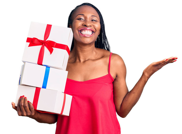 Young african american woman holding gift celebrating victory with happy smile and winner expression with raised hands  - Photo, image