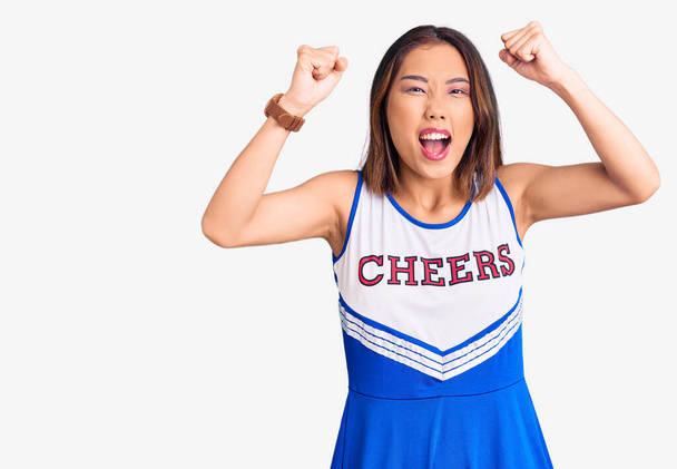 Young beautiful chinese girl wearing cheerleader uniform angry and mad raising fists frustrated and furious while shouting with anger. rage and aggressive concept.  - Photo, Image