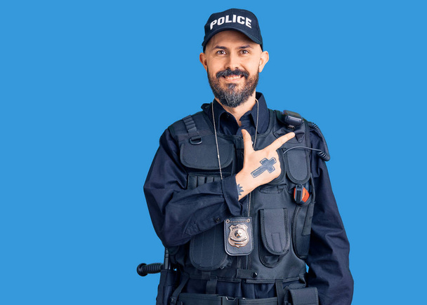 Joven hombre guapo vistiendo uniforme de policía alegre con una sonrisa en la cara señalando con la mano y el dedo hacia el lado con expresión feliz y natural  - Foto, Imagen