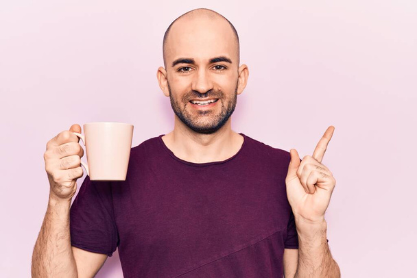 Молодий красивий лисий чоловік п'є чашку кави, посміхаючись щасливим вказуючи рукою і пальцем на бік
  - Фото, зображення