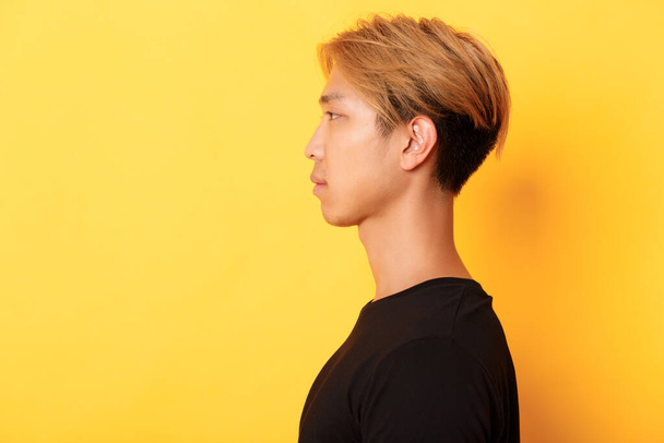 Φωτογραφία προφίλ του όμορφου κομψού κορεάτη άντρα που κοιτάζει αριστερά με σοβαρή έκφραση, στέκεται πάνω από το κίτρινο φόντο - Φωτογραφία, εικόνα