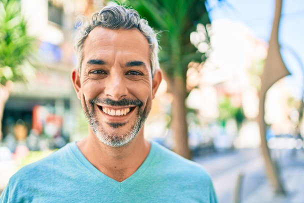 Homem de cabelos grisalhos de meia idade sorrindo feliz andando na rua da cidade. - Foto, Imagem